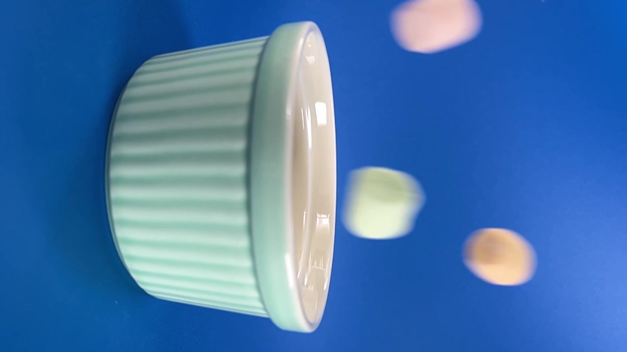 Slow motion close up of marshmallow dropping into ceramic ramekin against vibrant blue background for dessert, snack and food preparation concepts in Mexico