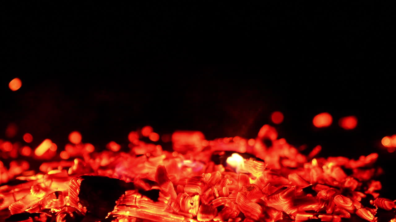 Beautiful smoldering embers in a pile. Tiny hot sparkles fly up into the darkness in the wind. Close up.