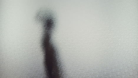 a female silhouette behind the frosted window touches the glass slowly