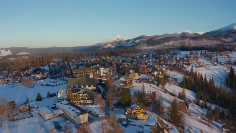 drone aerial shot of cyrhla in winter showing traditional houses, hotel and snowy peaks