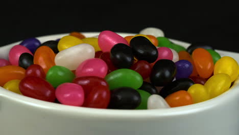 Weiße-Schüssel-Mit-Süßen-Jelly-Bean-Bonbons-Dreht-Sich-Auf-Schwarzem-Hintergrund