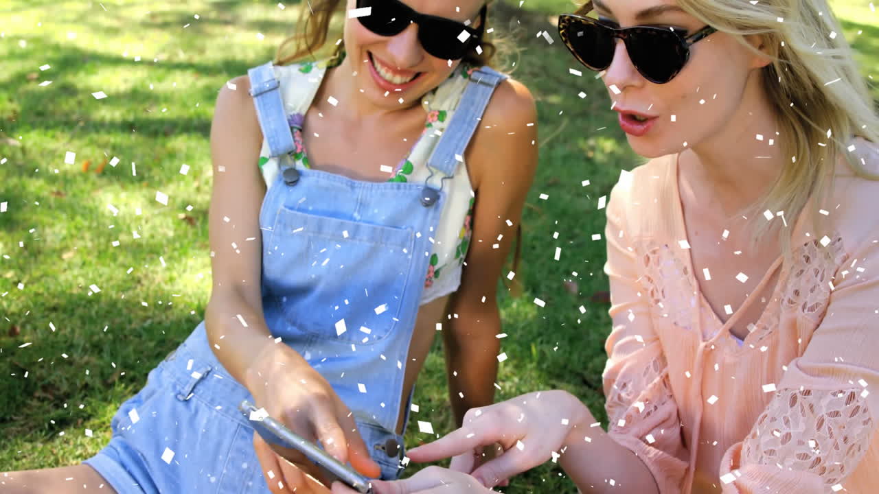 Wearing sunglasses, women celebrating outdoors with confetti falling around them