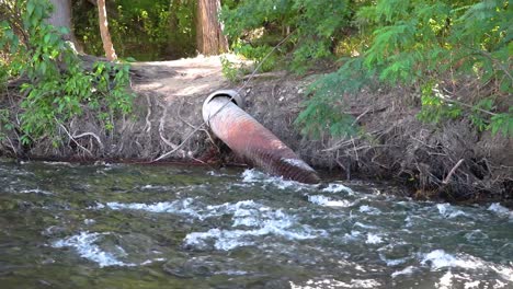 a metal irrigation pipe in a river flowing through the forest 10 second video.
