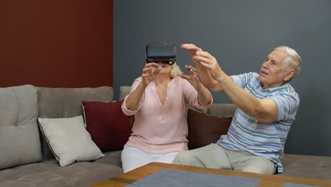 Senior-woman-playing-game-in-virtual-reality-headset-glasses,-man-laughing-with-her-action-at-home