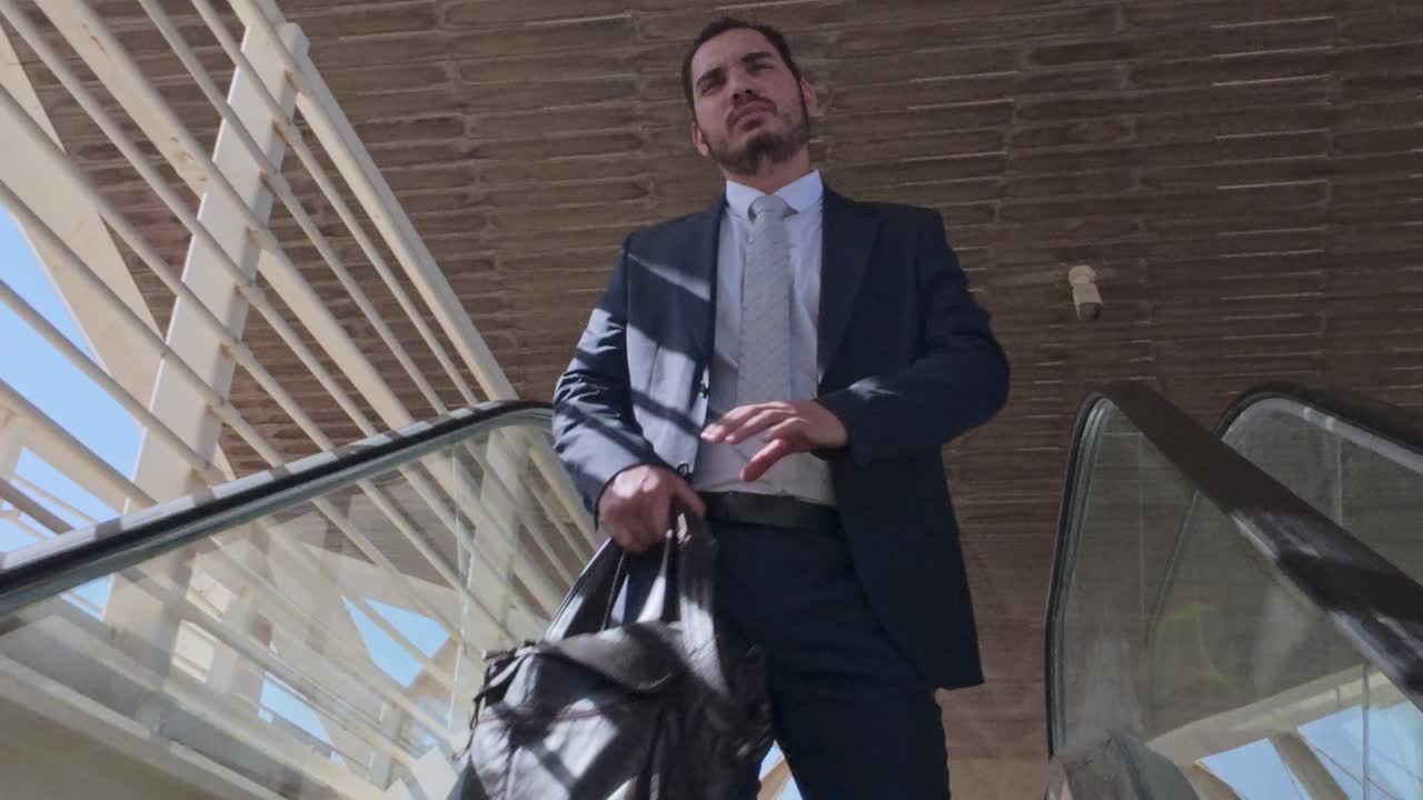 Empresario con maletín subiendo por una escalera mecánica en un edificio moderno
