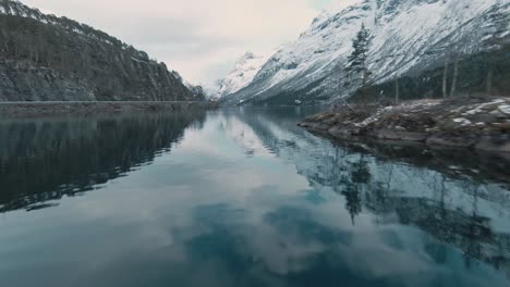 mountain range reflects in lake water in norway, loen, aerial fpv view