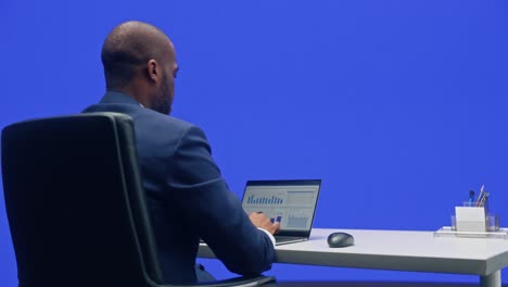 fondo de la oficina de pantalla verde: hombre de negocios negro sentado en su escritorio trabajando en una computadora portátil. hombre afroamericano trabajando con análisis de comercio electrónico de datos. disparo de seguimiento de 360 grados. moviéndose