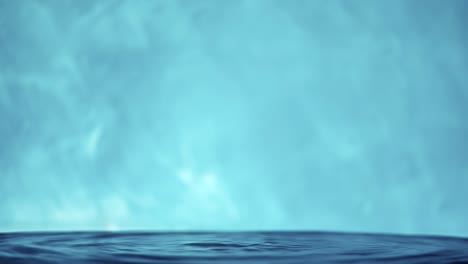 vídeo en 4k en cámara lenta de una superficie de agua con gotas que caen sobre un fondo azul. salpicaduras de agua. rodaje de estudio.