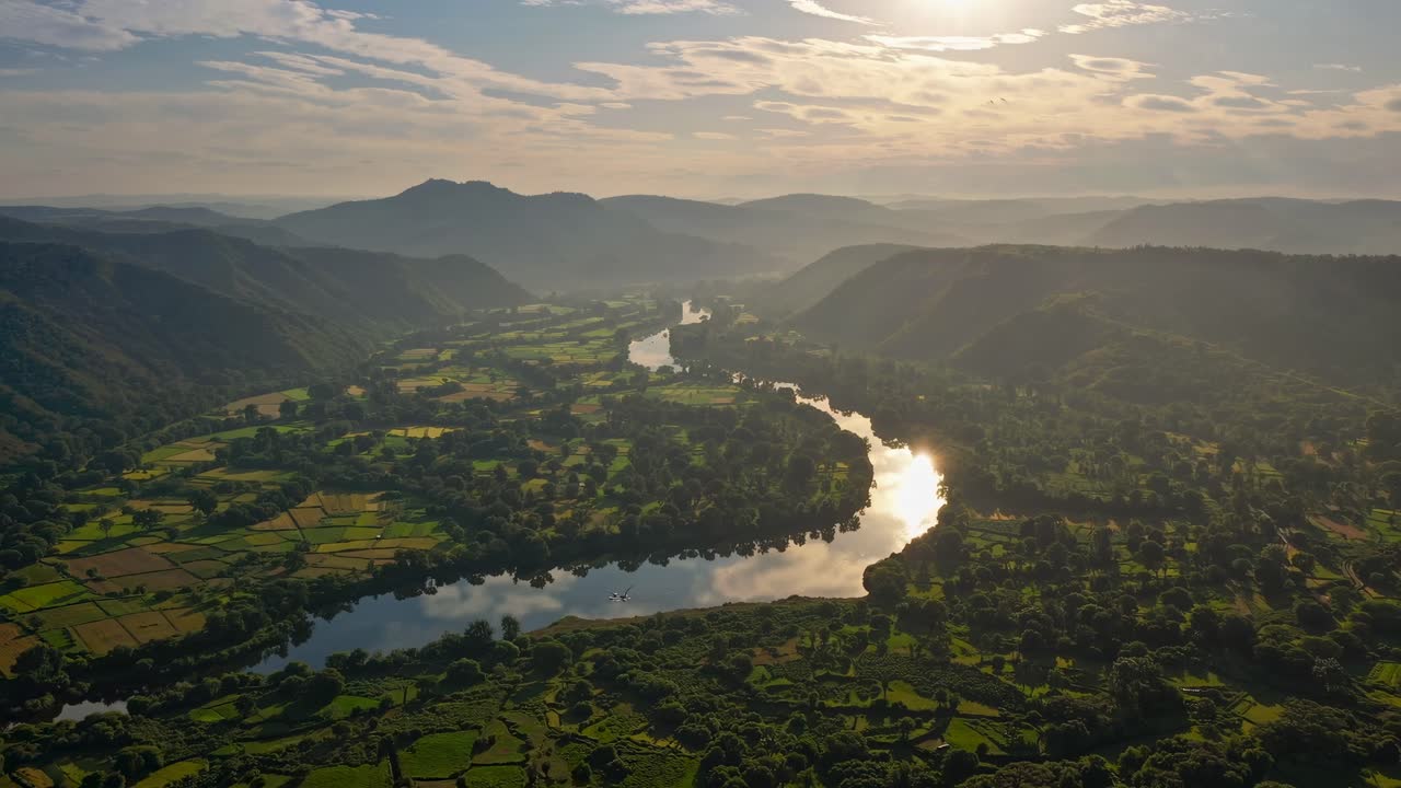 Aerial video captures a serene river winding through lush valleys at sunset, with mountains