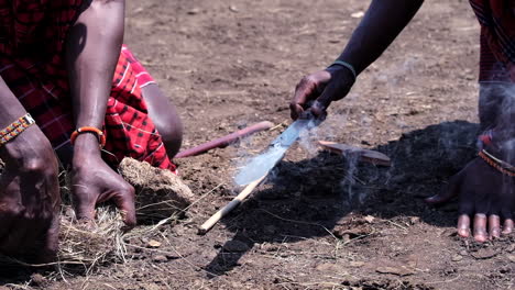 making fire: close-up of maasai hands creating fire with a stick and knife on dry ground