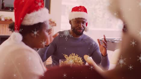 Yellow-star-icons-falling-against-african-american-man-talking-while-having-dinner-during-christmas