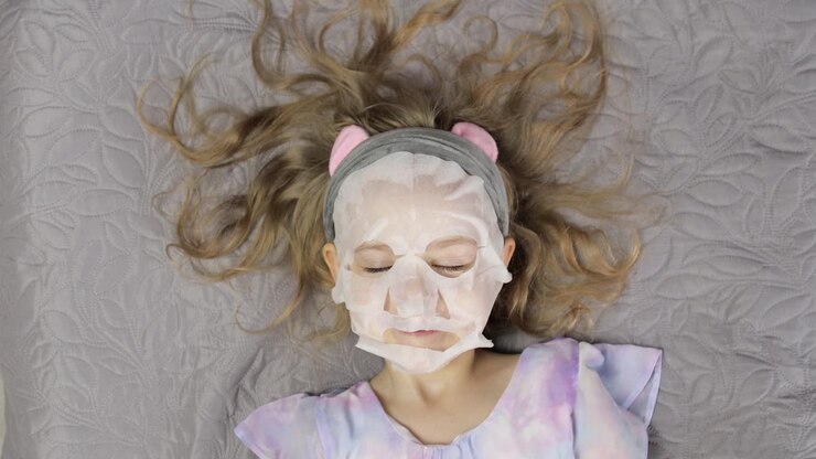 Teen girl applying moisturizing face mask. Child kid take care of skin with cosmetic facial mask