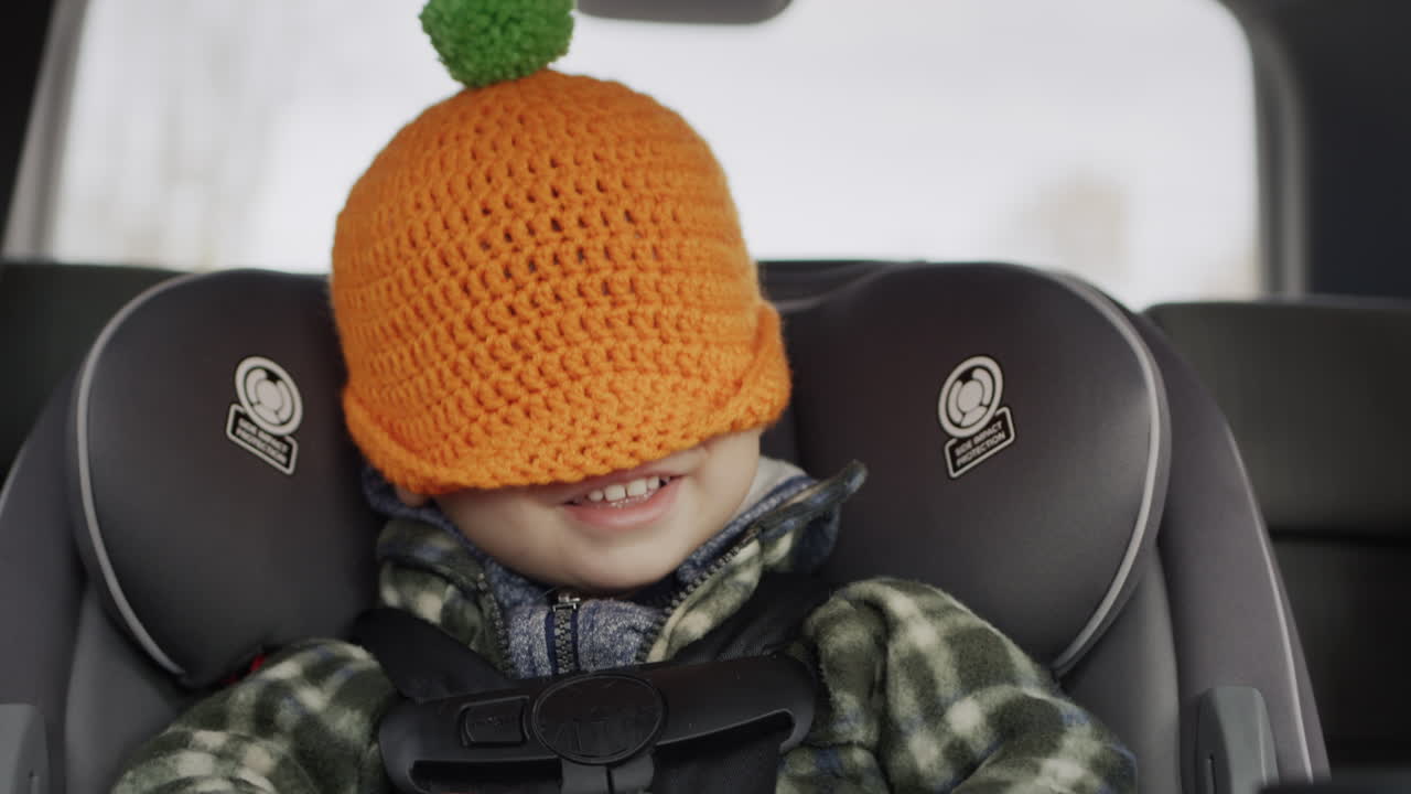 Un bambino allegro gioca a nascondino, si tira un cappello sulla testa. Viaggia su un seggiolino auto per bambini - un viaggio divertente con un bambino.