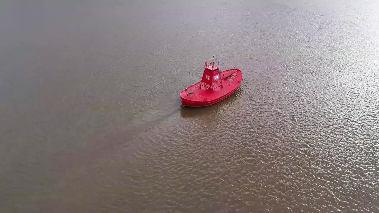 A brilliant red marker buoy in the river highlighting a safe navigation channel for shipping where shifting sands and sandbanks could leave a ship stranded at low tide.