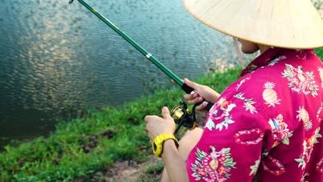 young mysterious man with conical hat and exotic shirt fishing in local pond, close up view