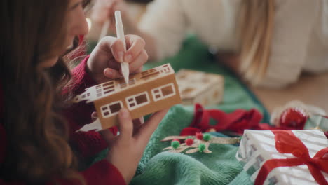 cropped sisters making cardboard house ornaments during christmas