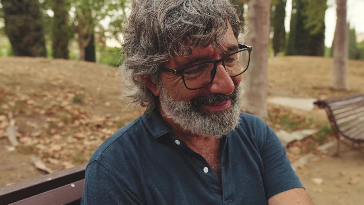Uomo maturo seduto su una panchina del parco che guarda verso il basso