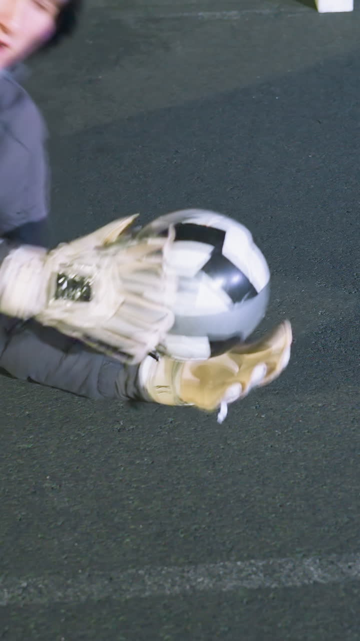 젊은 골키퍼는 강렬한 훈련 기간 동안 축구 공을 잡기 위해 왼쪽으로 뛰어들어, 밝은 아래에서 성공적인 세이브 후 땅에 누워있는 동안 결단력과 집중력을 보여줍니다.