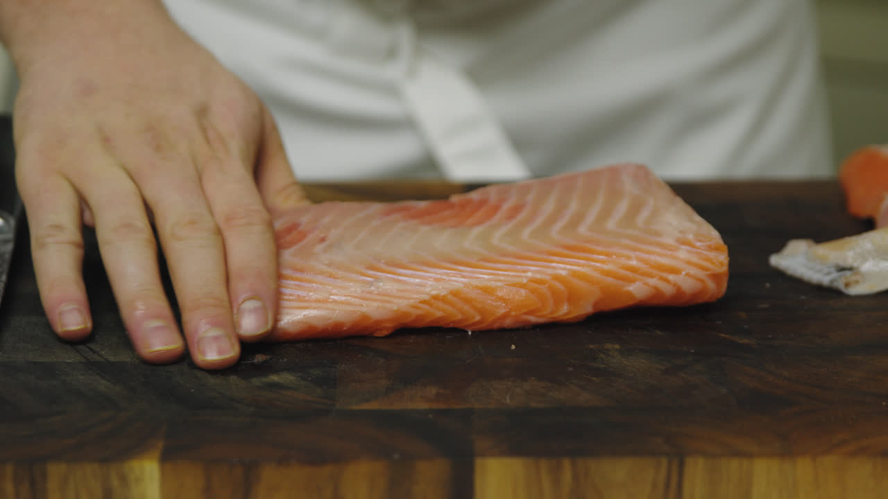 primer plano del chef pelando el filete de salmón en una tabla de madera en la cocina - descalcifique la piel del filete de salmón con un cuchillo afilado