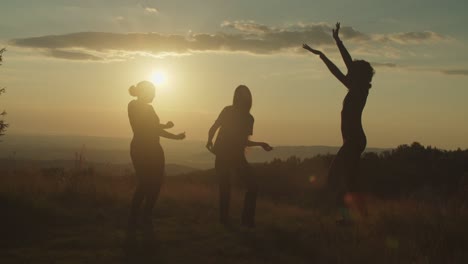 silhouette of elegant carefree women having fun dancing gracefully on mountain top at sunset