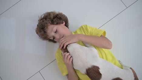 top view of a blond boy with curly hair lying on the floor and caresses his dog