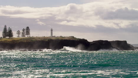 sun glaring onto the ocean below a lighthouse as the ocean moves in crisp slow motion