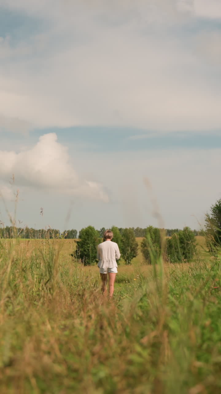 한 여인이 은 날 잔디을 고 다니며 손에 매달린 줄을 들고, 푸른 하늘 아래 멀리 있는 나무로 둘러싸인 넓은 야외 풍경에 둘러싸여 있습니다.