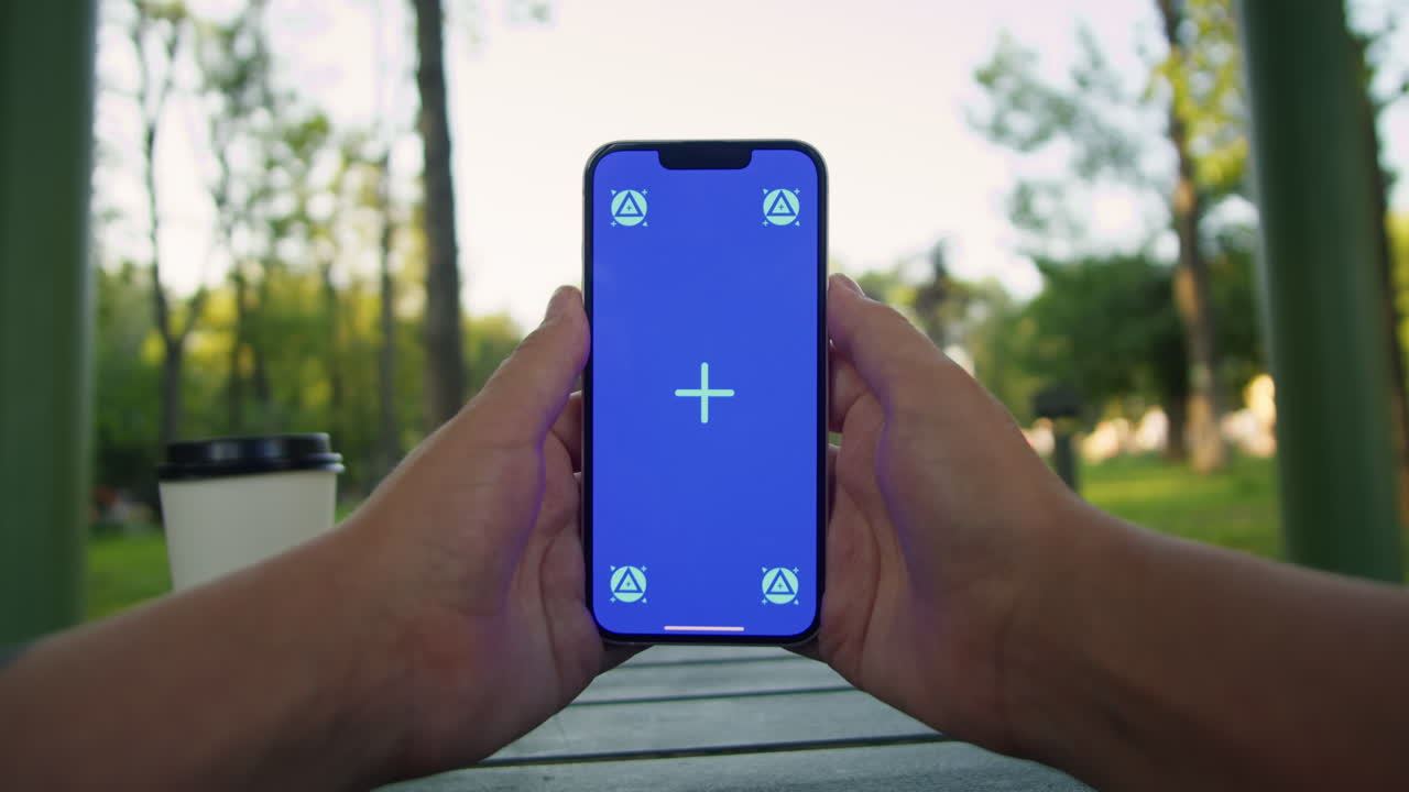 Young woman holding and swiping phone chroma key screen in the park in front of trees close-up. Girl with green screen on smart phone. Nature