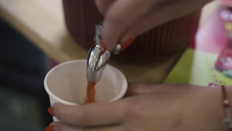 Close-up-of-a-hand-pouring-juice-into-a-paper-cup