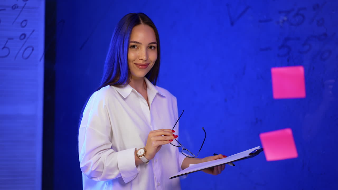 Young adult preparing for a meeting. Young woman holding a clipboard stands in a blue-lit room surrounded by notes and charts, preparing for a discussion