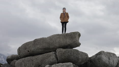 a girl stands on boulders with snowy mountains around her.