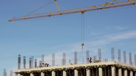 construction site with workers over terrace loading tower crane ballet with bricks on blue sky background, wide static shot