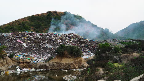 Close-up of heap of smoking rubbish in an open-air dump in middle of hill with sewage
