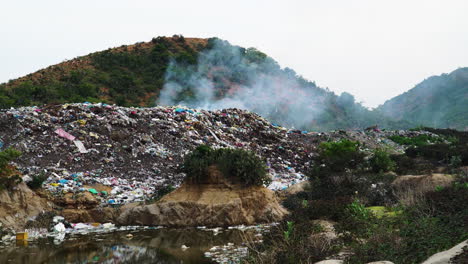 close-up of heap of smoking rubbish in an open-air dump in middle of hill with sewage