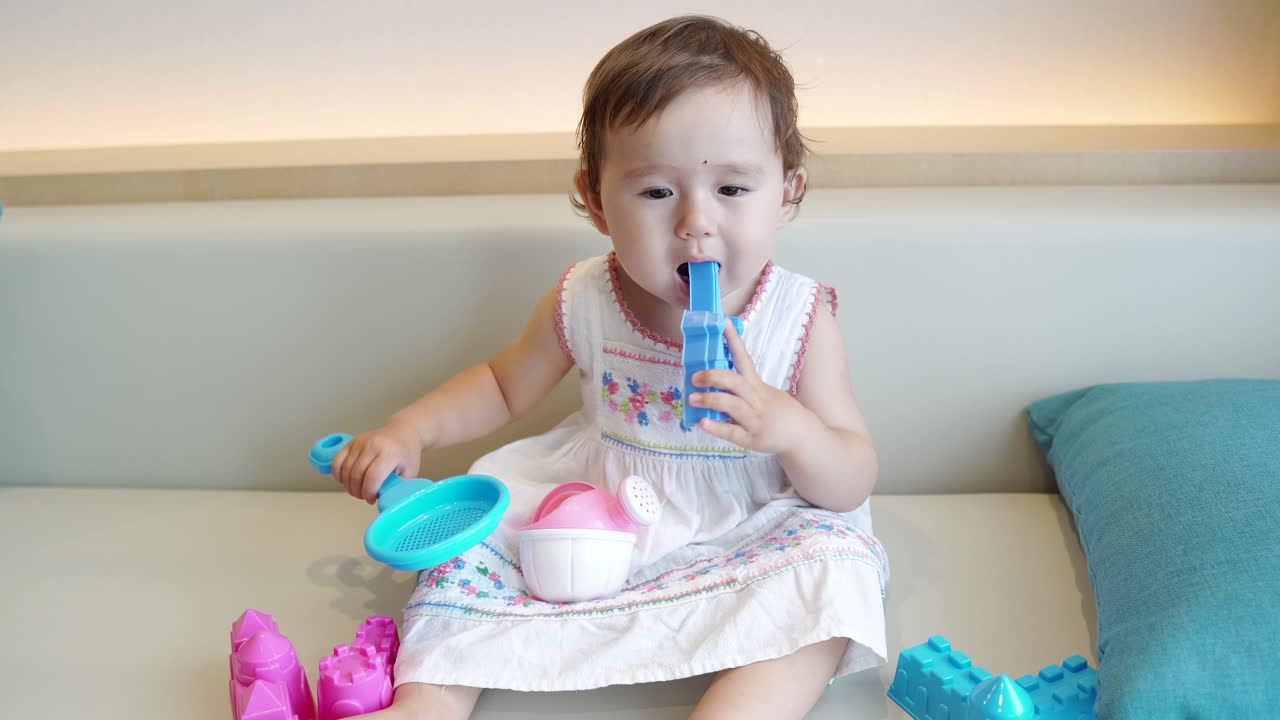 Curious Toddler Girl Playing And Chewing Her Toys In A Sofa