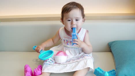 curious toddler girl playing and chewing her toys in a sofa