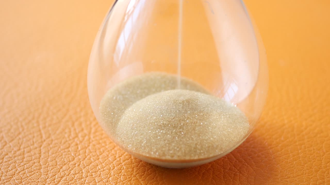 reloj de arena en la mesa, arena fluyendo a través de la bombilla de vidrio de arena