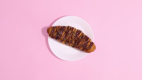delicious chocolate croissant move on white plate on pastel pink background. stop motion