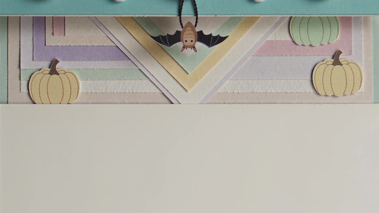 Mani che tirano fili sollevando una striscia color ottanio con perline e un pipistrello su un tavolo da lavoro, rivelando un biglietto color crema