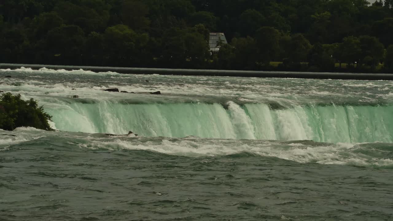 Low-angle shot of rapids tumbling into the falls. Trees and greenery frame the edge