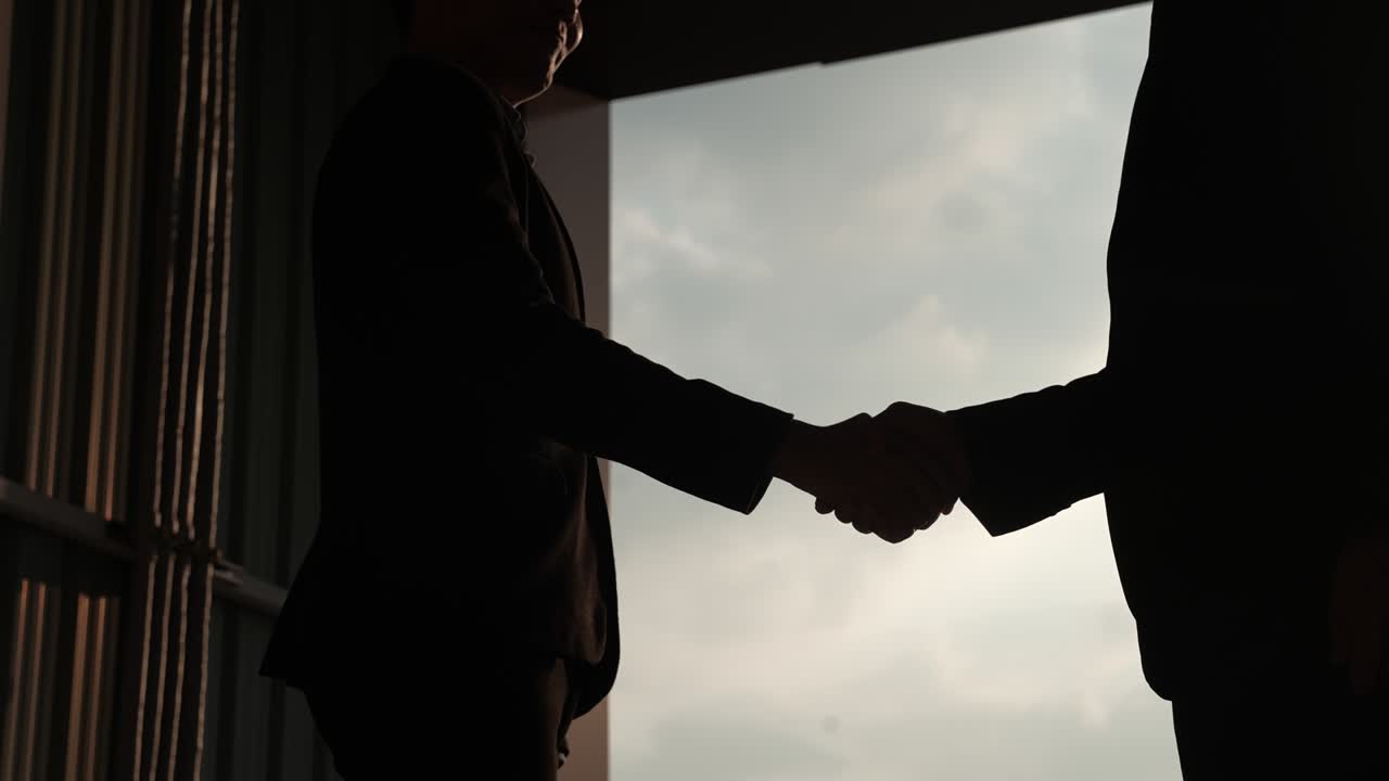 Silhouette of 2 businessmen shake hands to join the business at sunset, business partner concept, shot slow-motion 4k