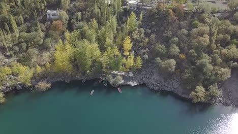 birds eye rising view of boats moored along kachura lake skardu coastline with tilt up reveal gilgit-baltistan landscape