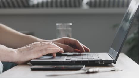 an unrecognizable man uses mobile internet from his smartphone to work on a laptop.