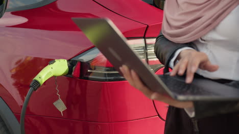 businesswoman working on a laptop while charging an electric car