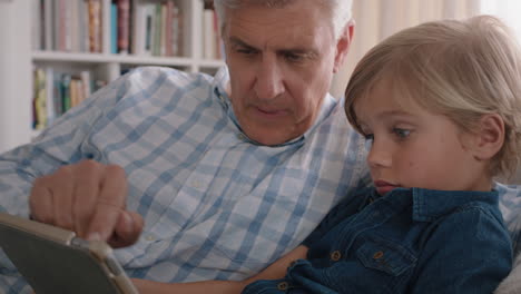 abuelo mostrando a un niño pequeño cómo usar una computadora tablet enseñando a un nieto curioso tecnología moderna niño inteligente aprendiendo dispositivo móvil sentado con el abuelo en el sofá 4k