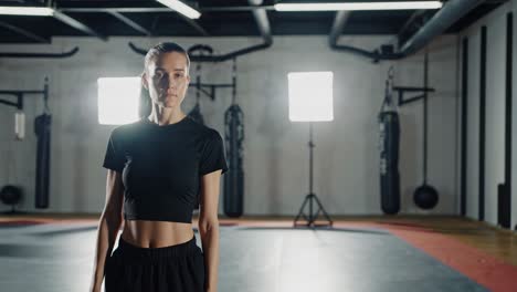 young woman in sportswear standing confidently in a gym, surrounded by fitness equipment and bright lights, ready to begin her training session