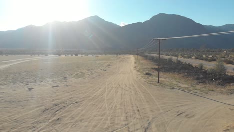 Antena-De-Bajo-Vuelo-Siguiendo-Algunas-Líneas-Eléctricas-A-Lo-Largo-De-Un-Camino-De-Tierra-En-El-Desierto