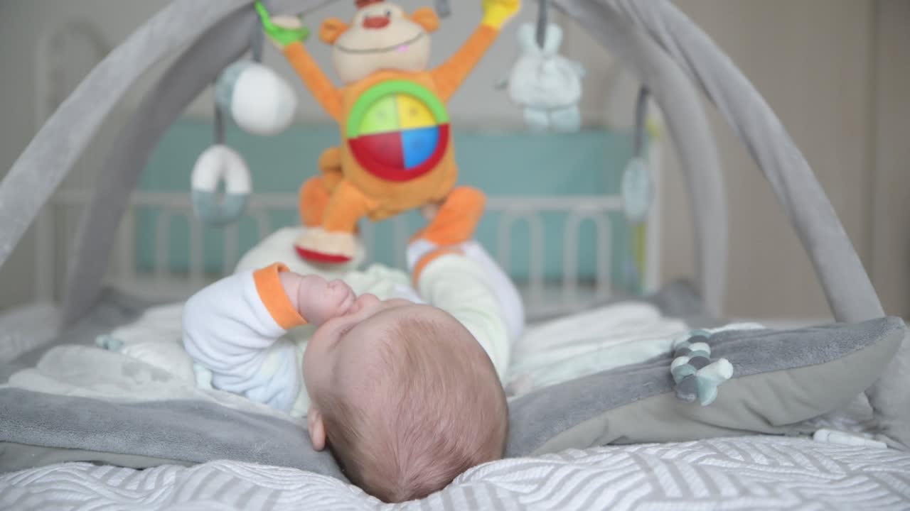 Bambino che gioca con giocattoli appesi su un tappeto per lo sviluppo.