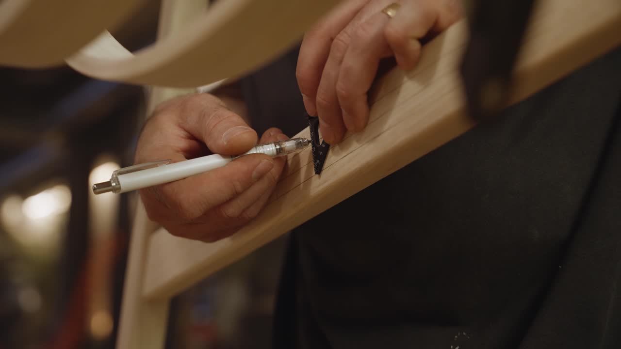 Close-up of a craftsman drawing precise lines on a wooden piece using a metal ruler and pen, highlighting accuracy, focus, and traditional woodworking craftsmanship