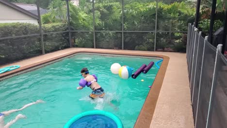 young boy with inflatable bracelets jumps into the swimming pool in slow motion